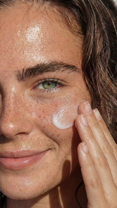 Close-up of woman applying daily cleanser or anti-aging skincare cream to her cheek