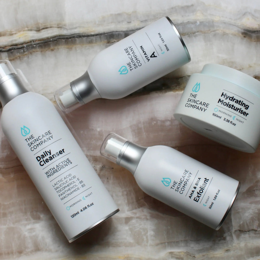 Four anti-aging skincare products including daily cleanser, exfoliant, Vitamin A serum, and hydrating moisturiser on a marble surface.