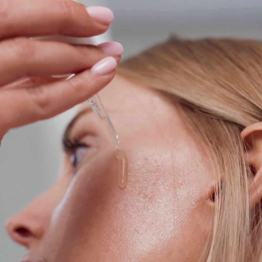 Woman applying vitamin C serum to cheek with dropper, skincare routine close-up