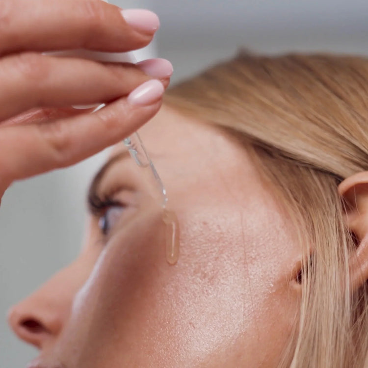 Woman applying vitamin C serum to cheek with dropper, skincare routine close-up